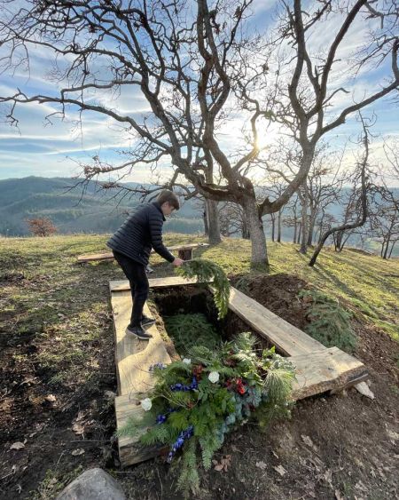 youth gently lays green pine boughs on natural burial grave