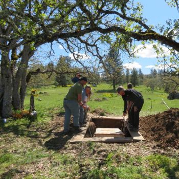 gently lowering wood casket into grave during natural burial